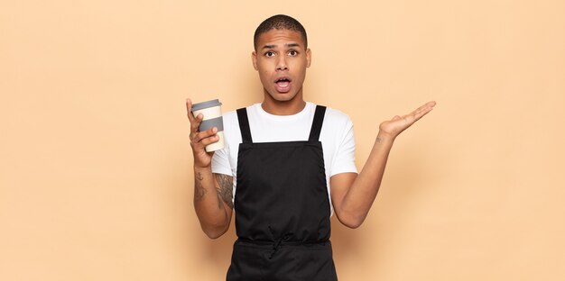 Young black man looking surprised and shocked, with jaw dropped holding an object with an open hand on the side