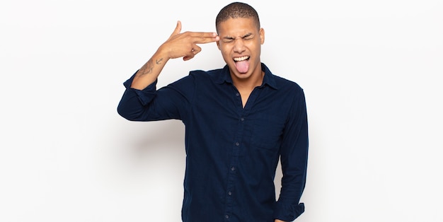 Young black man looking unhappy and stressed, suicide gesture making gun sign with hand, pointing to head