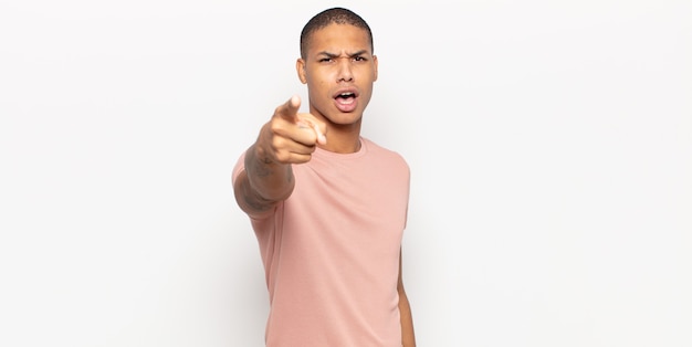 Young black man pointing at camera with an angry aggressive expression looking like a furious, crazy boss