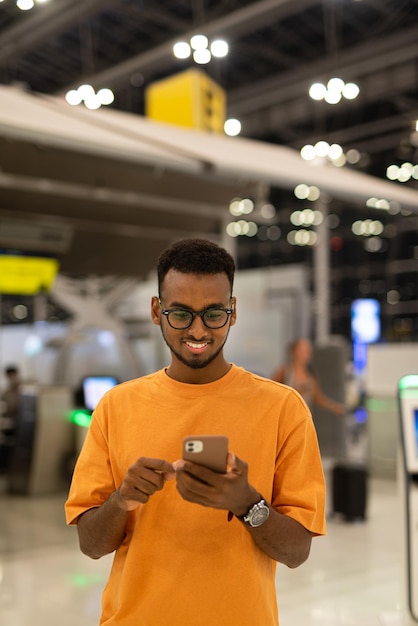 Young black man ready to travel at airport terminal waiting for flight while using phone