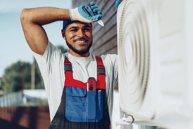 Young black man repairman checking an outside air conditioner unit