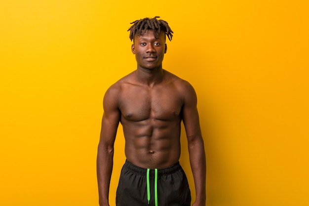 Young black man shirtless wearing swimsuit happy, smiling and cheerful.