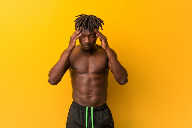 Young black man shirtless wearing swimsuit touching temples and having headache.