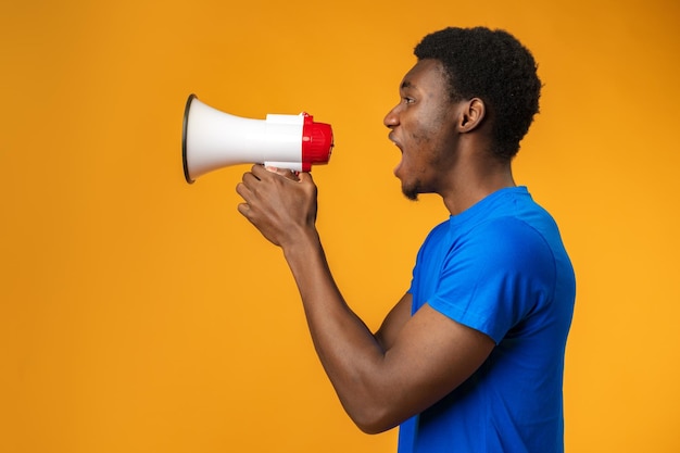 Young black man shouting in megaphone on yellow background