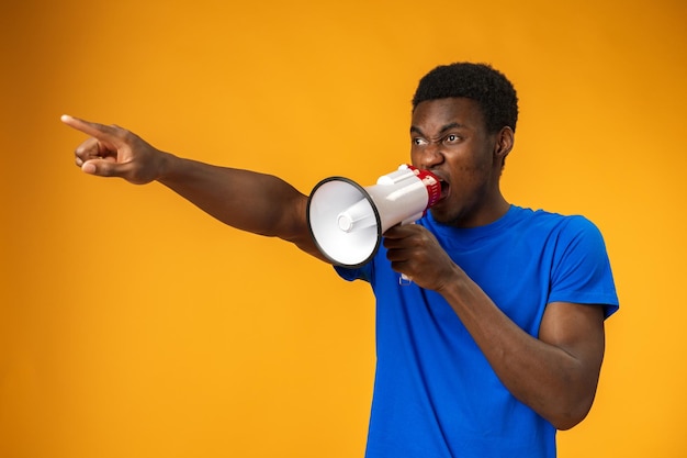 Young black man shouting in megaphone on yellow background