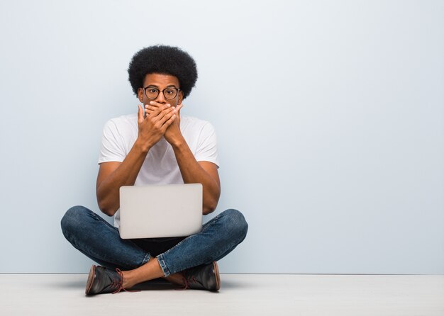 Young black man sitting on the floor with a laptop surprised and shocked