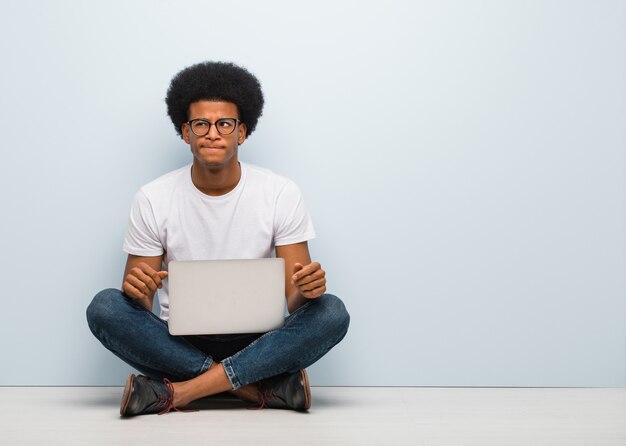 Молодой черный человек сидит на полу с ноутбуком, думая об идее