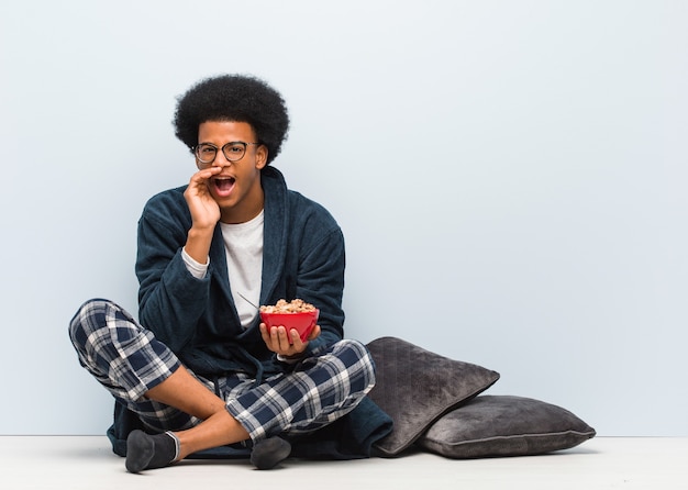 Giovane uomo di colore seduto e fare colazione gridando qualcosa di felice di fronte