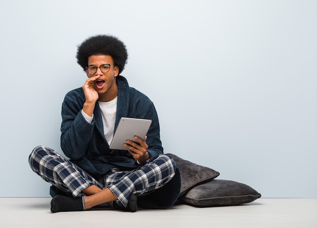 Young black man sitting on his house and holding his tablet shouting something happy to the front