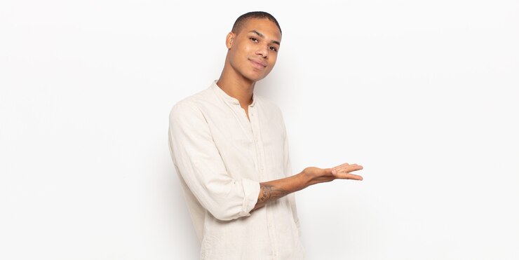 Photo young black man smiling cheerfully, feeling happy and showing a concept in copy space with palm of hand