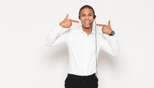 Young black man smiling confidently pointing to own broad smile, positive, relaxed, satisfied attitude