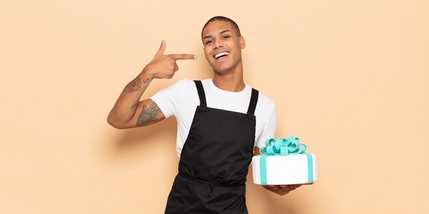 Young black man smiling confidently pointing to own broad smile, positive, relaxed, satisfied attitude