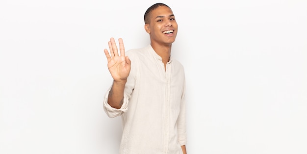 Young black man smiling happily and cheerfully, waving hand, welcoming and greeting you, or saying goodbye