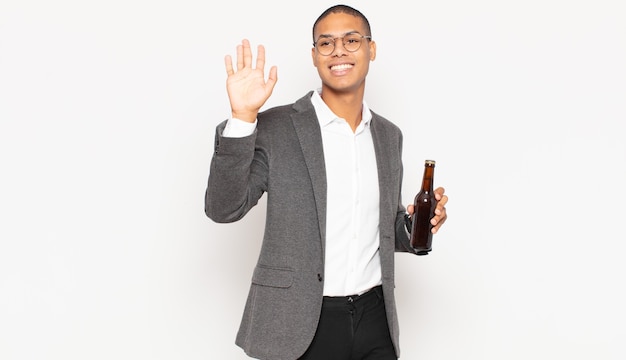 Young black man smiling happily and cheerfully, waving hand, welcoming and greeting you, or saying goodbye