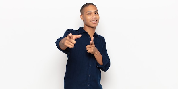 Young black man smiling with a positive, successful, happy attitude pointing to the camera, making gun sign with hands