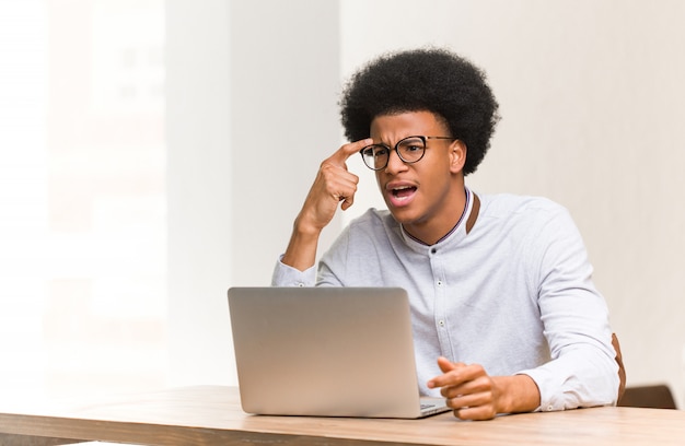 Young black man using his laptop doing a disappointment gesture with finger