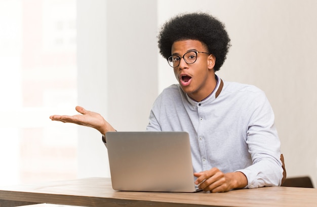 Young black man using his laptop holding something on palm hand