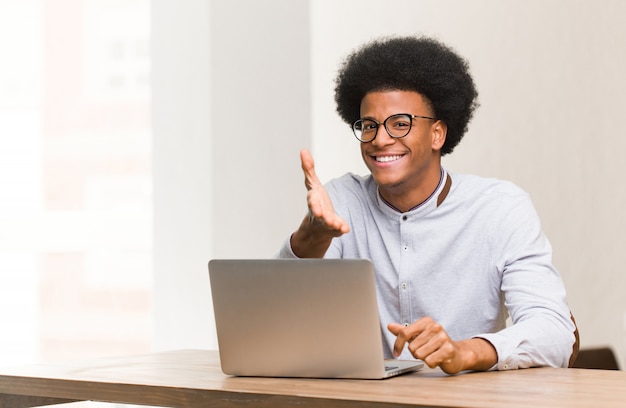 Giovane uomo di colore che utilizza il suo laptop che raggiunge fuori per accogliere qualcuno