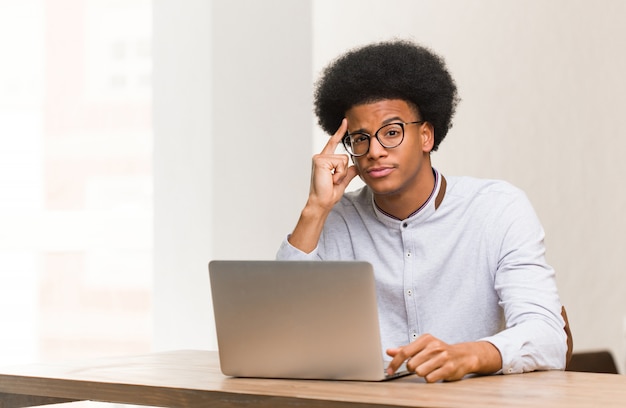 Giovane uomo di colore che per mezzo del suo computer portatile che pensa ad un'idea