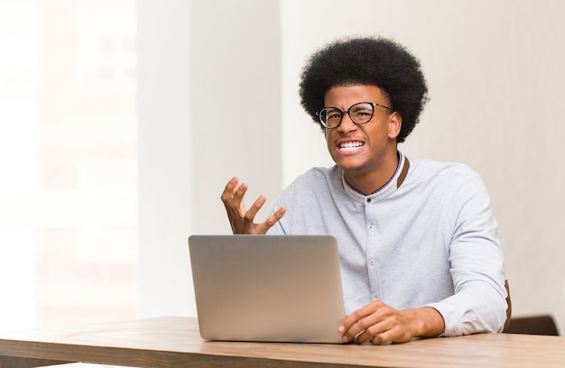 Giovane uomo di colore usando il suo laptop molto spaventato e impaurito