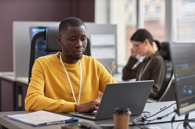 Young black man using laptop while working as software developer in IT company