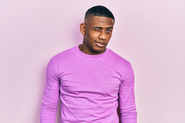 캐주얼 핑크색 스웨터를 입은 젊은 흑인 남자가 섹시하고 명랑하고 행복한 얼굴로 카메라를 바라보며 윙크하고 있다