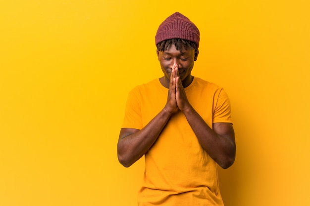 Young black man wearing dreads holding hands in pray near mouth, feels confident.