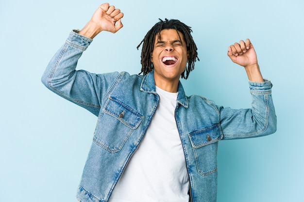 Young black man wearing a jeans jacket celebrating a special day, jumps and raise arms with energy.