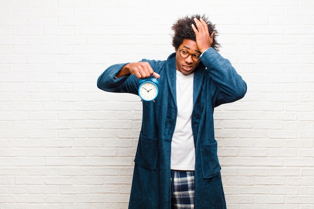 Young black man wearing pajamas with an alarm clock