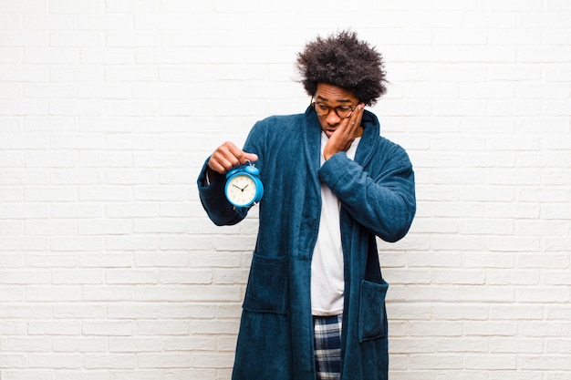 Young black man wearing pajamas with an alarm clock