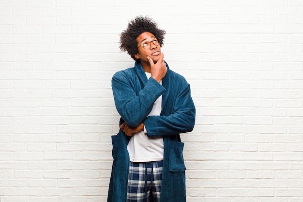 Young black man wearing pajamas with gown feeling thoughtful, wondering or imagining ideas, daydreaming and looking up to copy space