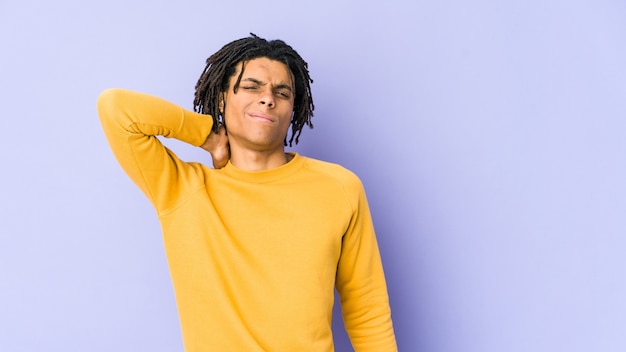 Young black man wearing rasta hairstyle having a neck pain due to stress, massaging and touching it with hand.