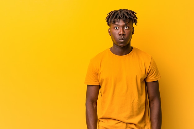 Young black man wearing rastas blows cheeks, has tired expression. Facial expression concept.