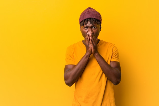 Young black man wearing rastas over yellow background scared and afraid.