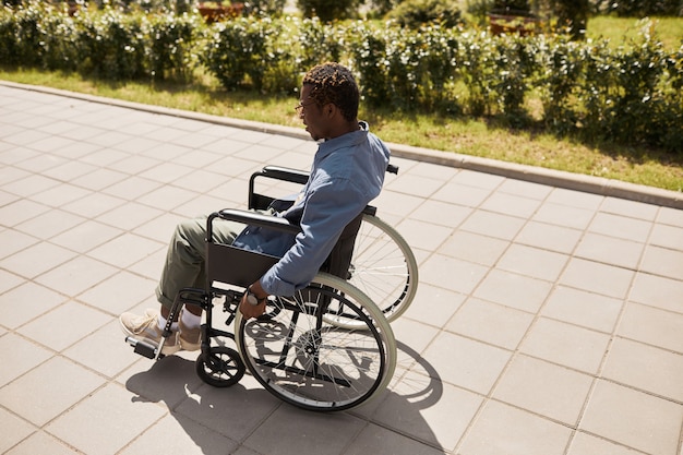 Photo young black man with aching legs moving forward in wheelchair over street, rehab concept