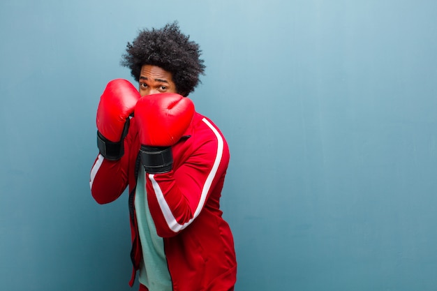 Young black man with boxing gloves against blue grunge wall