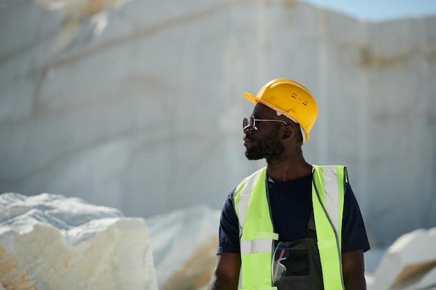 Young black man in workwear eyeglasses and protective helmet on quarry