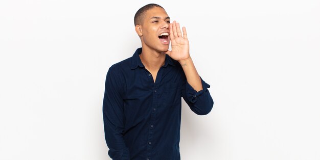 Young black man yelling loudly and angrily to copy space on the side, with hand next to mouth