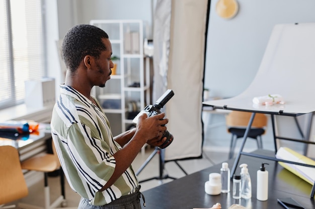 Молодой черный фотограф в студии, вид сбоку