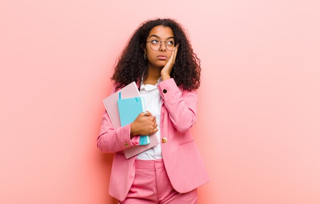 Young black pretty business woman with books against pink wall wall