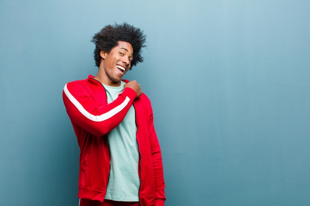 Young black sports man feeling happy, positive and successful, motivated when facing a challenge or celebrating good results on grunge wall