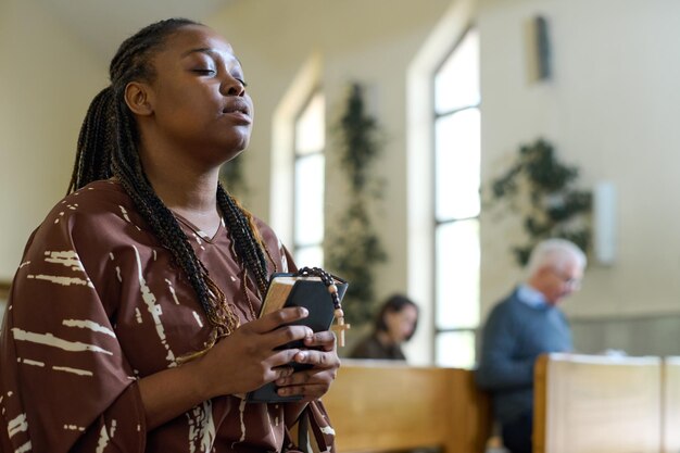 Photo young black woman in casual dress keeping her eyes closed during prayer