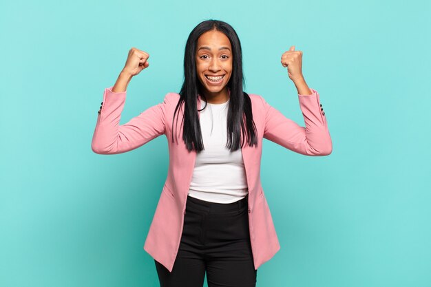 Молодая чернокожая женщина празднует невероятный успех как победитель, выглядит взволнованной и счастливой, говоря: «возьми это!». бизнес-концепция