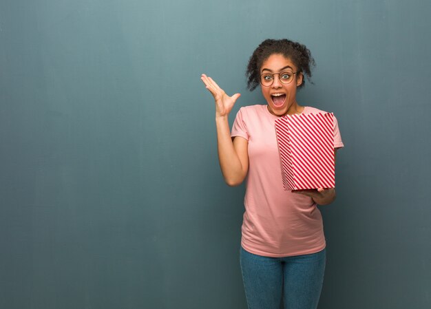 Young black woman celebrating a victory or success. She is holding a popcorns bucket.