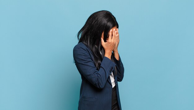 Young black woman covering eyes with hands with a sad, frustrated look of despair, crying, side view. business concept