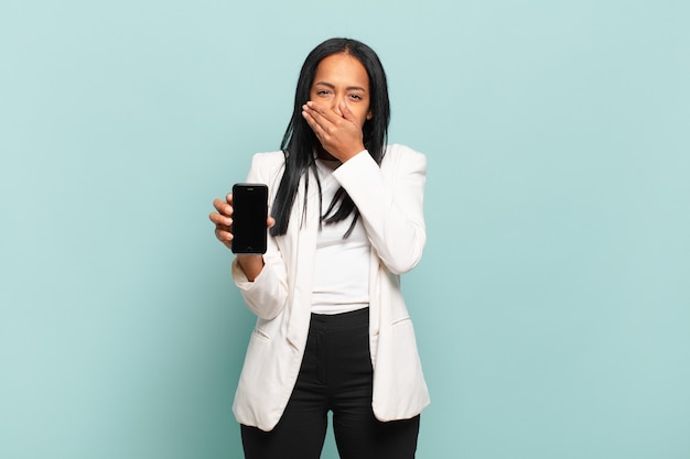 Young black woman covering mouth with hands with a shocked, surprised expression, keeping a secret or saying oops. smart phone concept