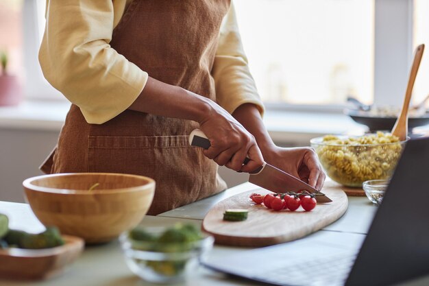 Foto giovane donna nera che taglia le verdure cucinando con alimenti biologici in cucina