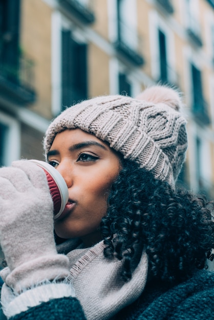 겨울에 마드리드의 거리에서 방황하는 커피를 마시는 젊은 흑인 여성
