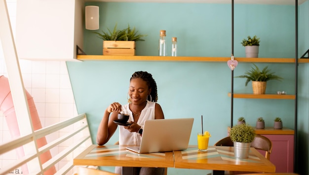 Giovane donna di colore che beve caffè mentre lavora al computer portatile nella caffetteria