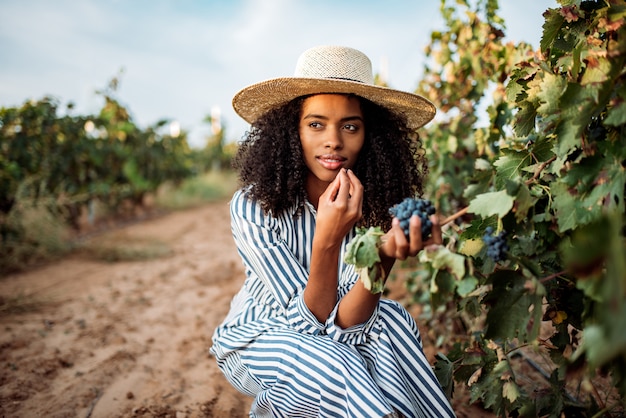 Young black woman eating a grape in a vineyard